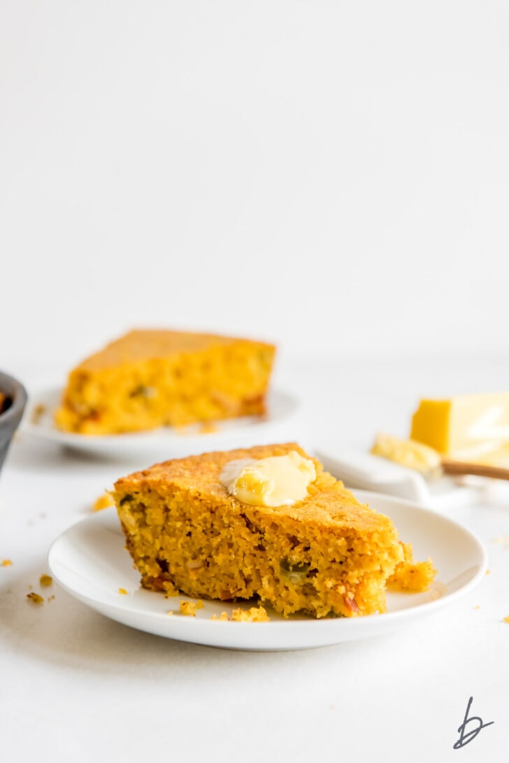 slice of jalapeno cheese cornbread with melted butter on white round plate