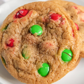 white plate with red and green m&m christmas cookie leaning on another cookie