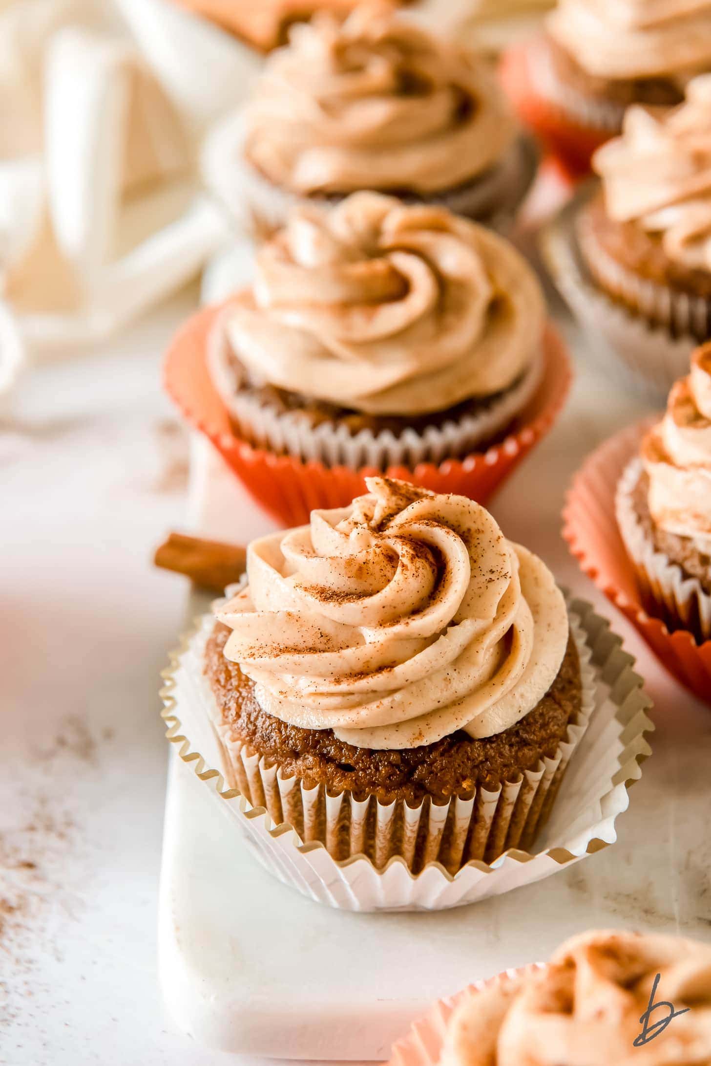 pumpkin cupcake with cream cheese frosting on open paper liner with more cupcakes behind it