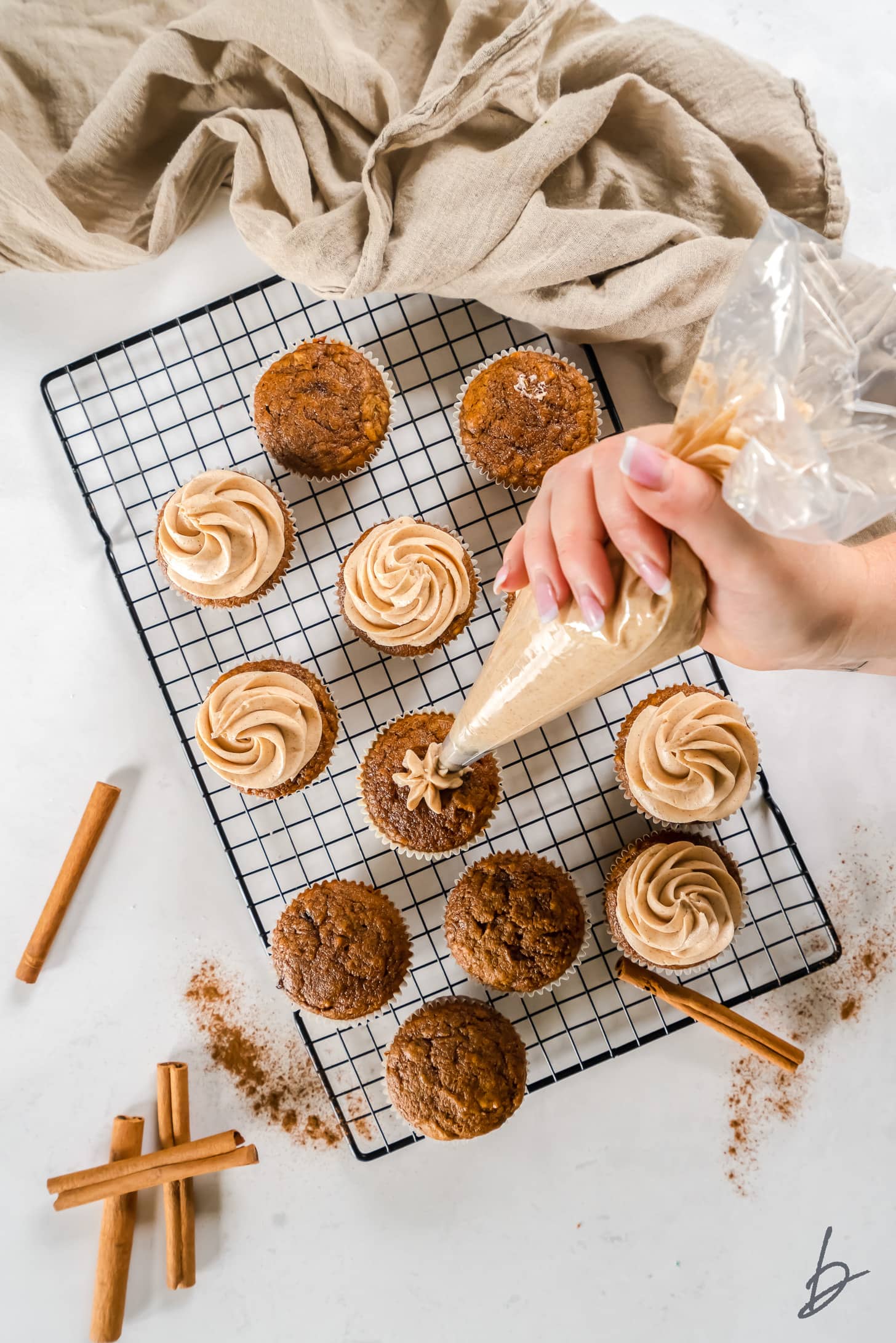 hand holding frosting bag and frosting pumpkin cupcakes on wire cooling rack