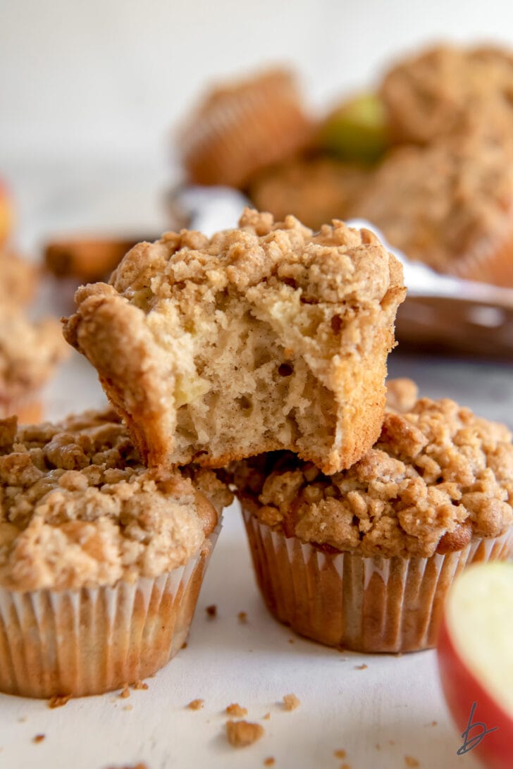 apple crumble muffin with a bite on top of two other muffins