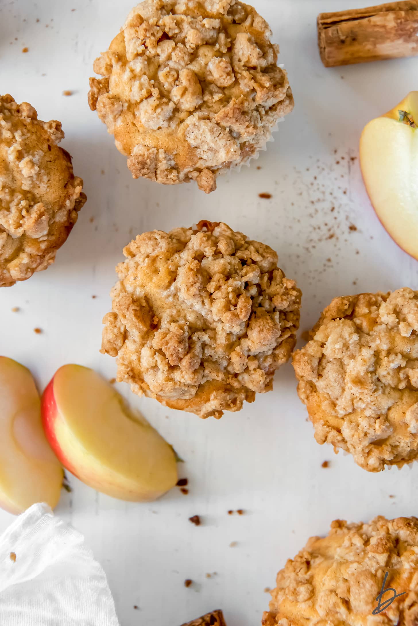 tops of apple crumble muffins on surface next to apple slices and cinnamon stick.