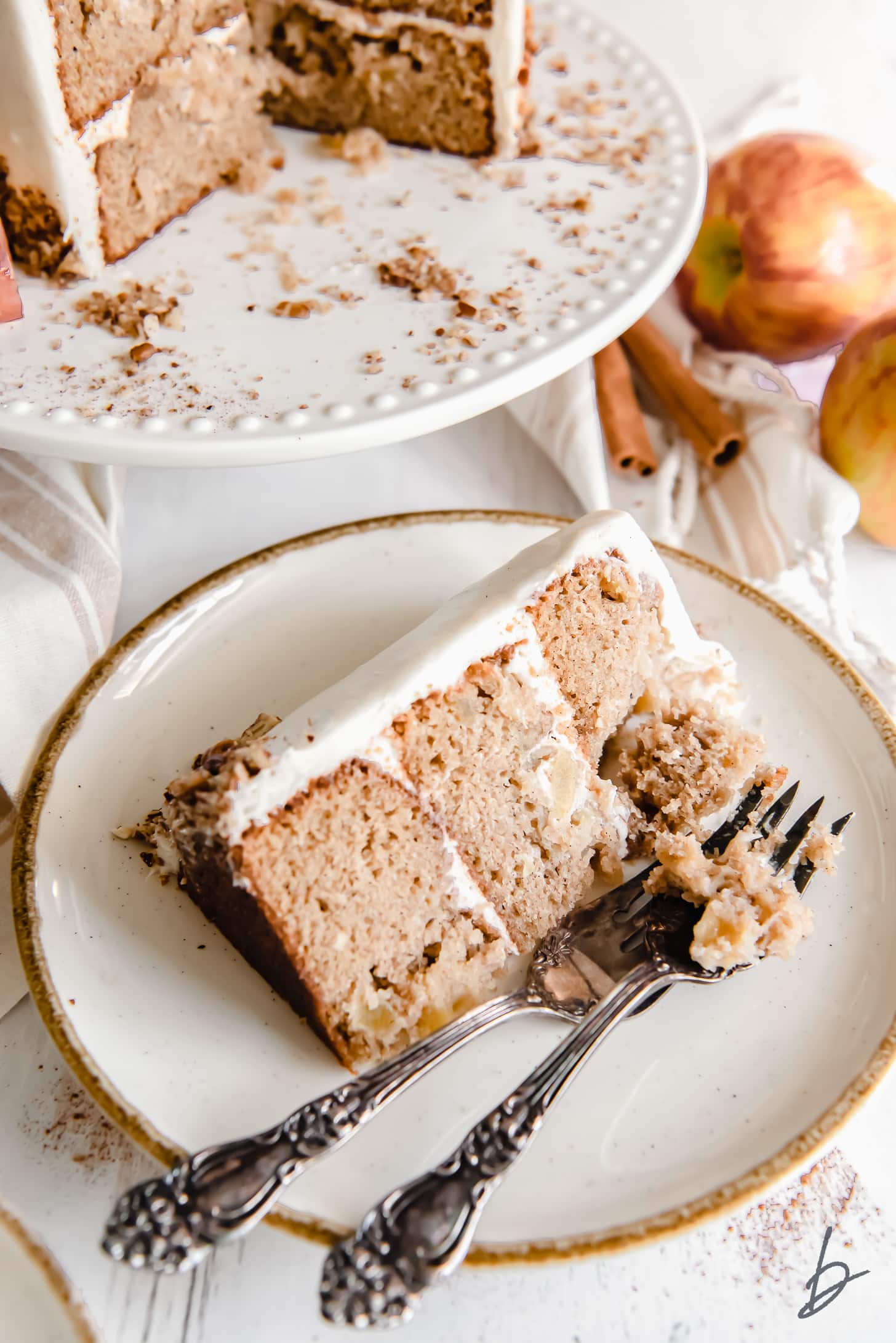 slice of triple layer apple spice cake on white gold-rimmed plate with two forks