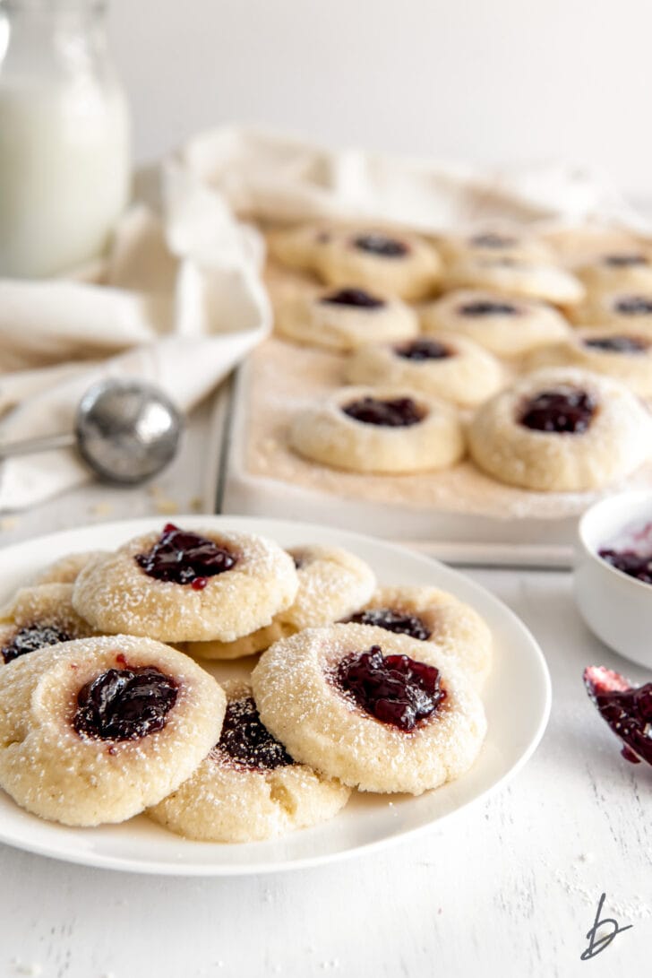 plate of jam thumbprint cookies in front of cookie sheet with more cookies