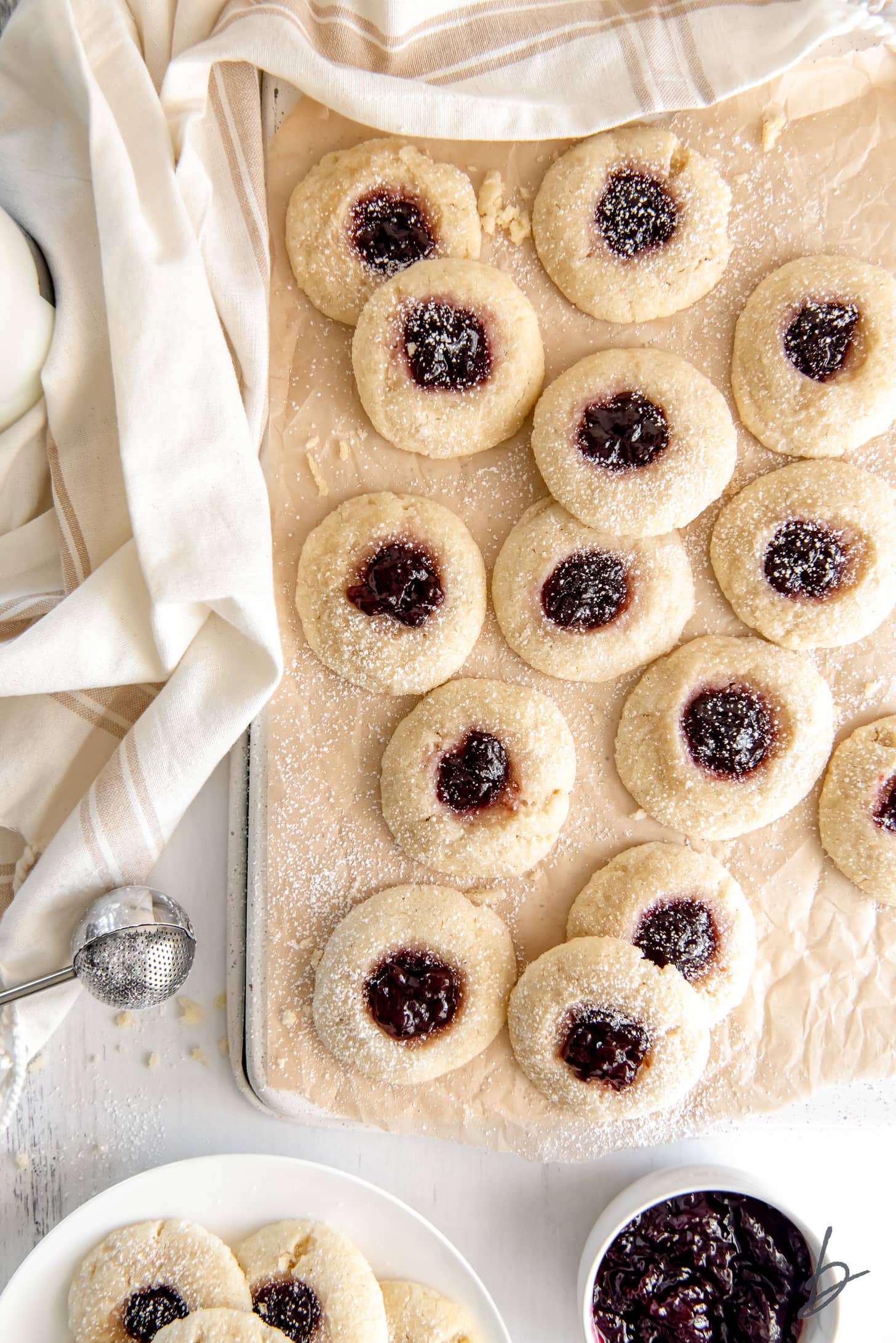 jam thumbprint cookies on parchment paper next to cream-colored kitchen cloth