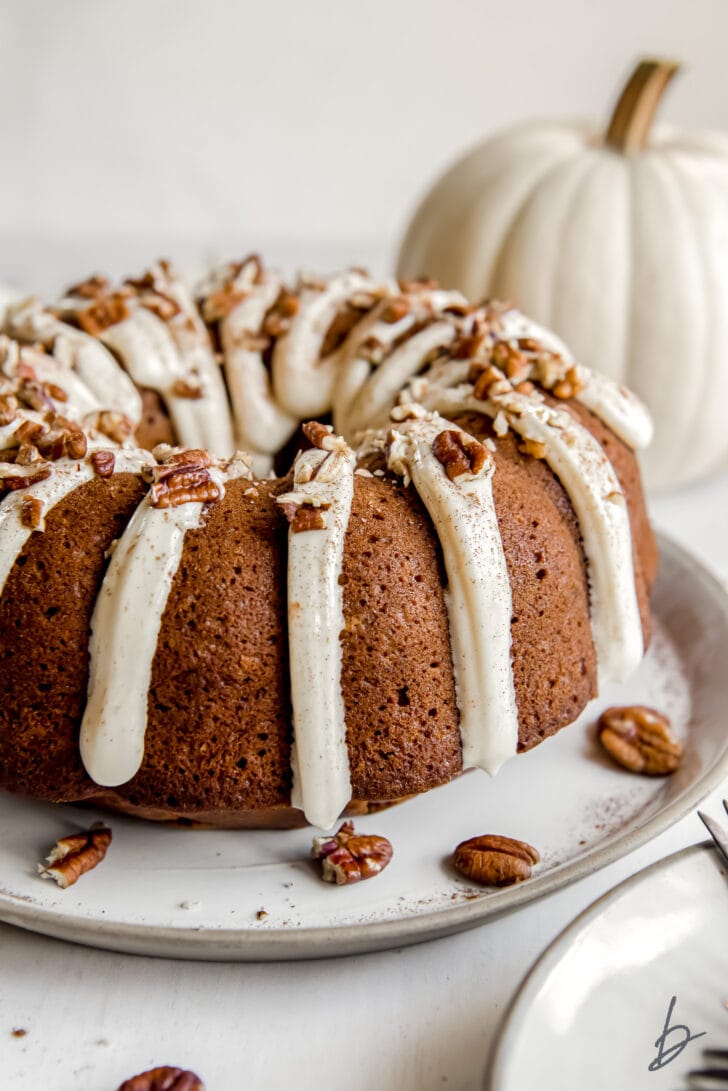 pumpkin bundt cake with cream cheese frosting dripping down side and chopped pecans on top
