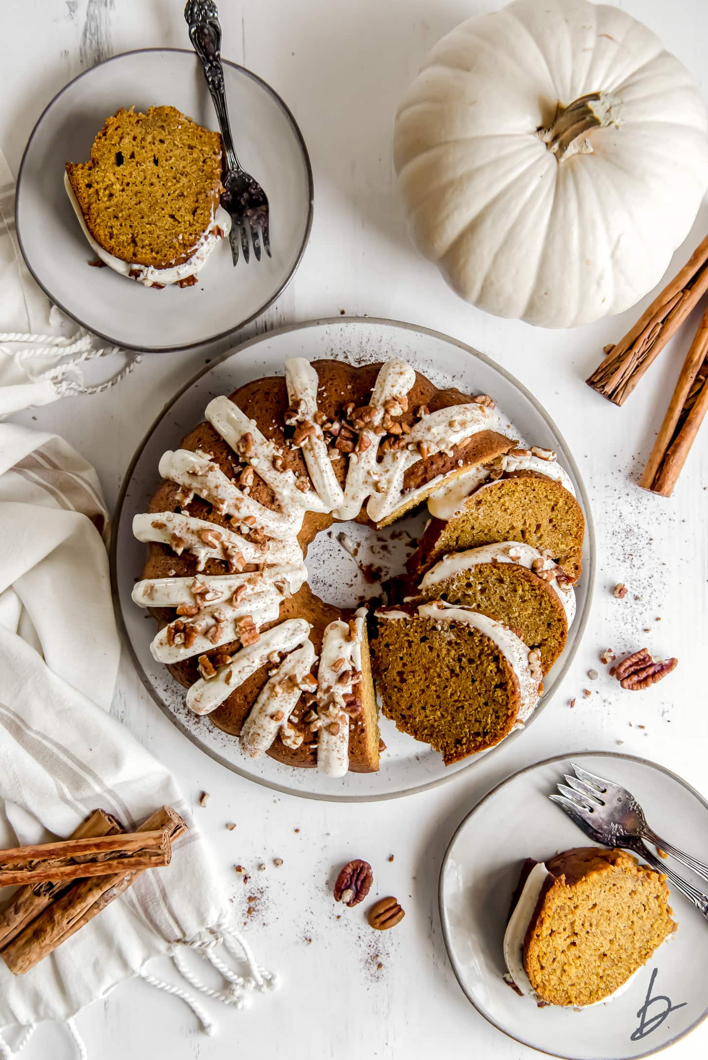 pumpkin bundt cake on plate next to a white pumpkin two smaller plates with cake slices