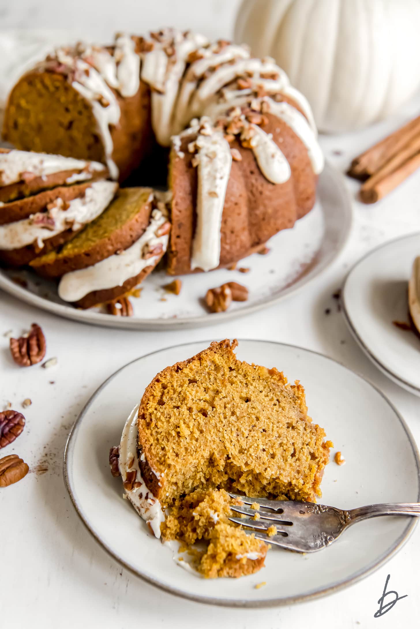 pumpkin bundt cake slice on plate with fork taking bite and full cake behind cake slice