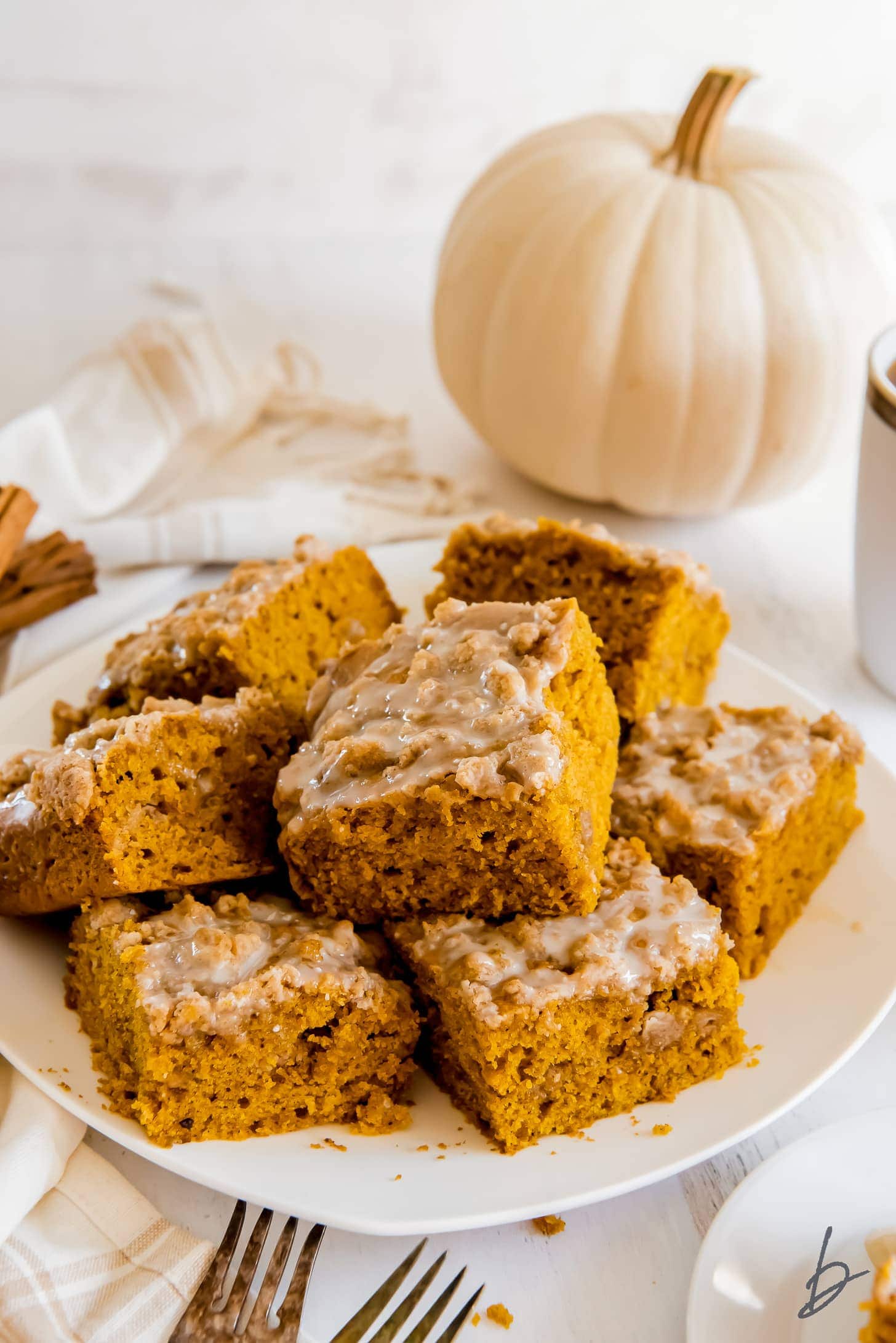 plate of pumpkin coffee cake square with icing and white pumpkin behind plate