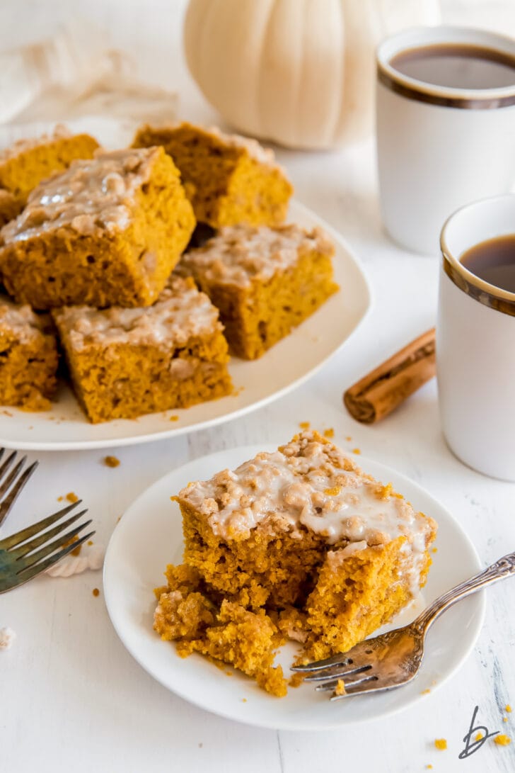fork taking bite of pumpkin coffee cake on small white plate with larger plate with more coffee cake behind it