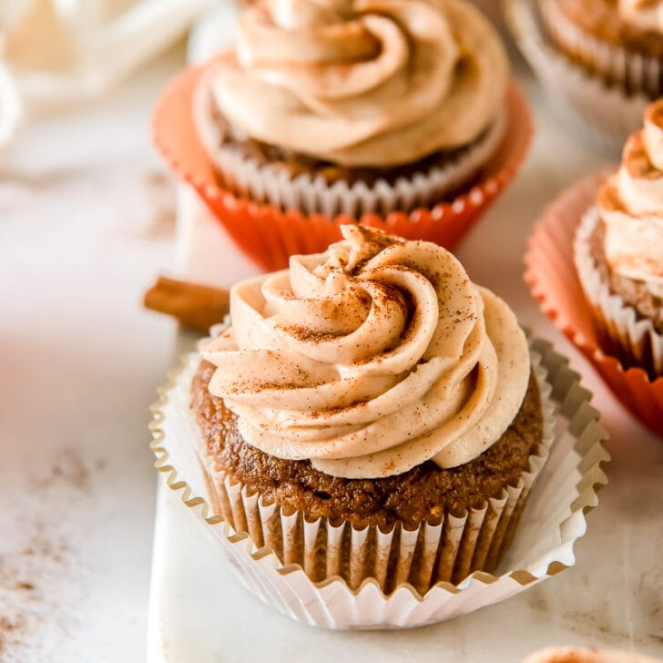 pumpkin cupcake with cinnamon cream cheese frosting on open paper cupcake liner