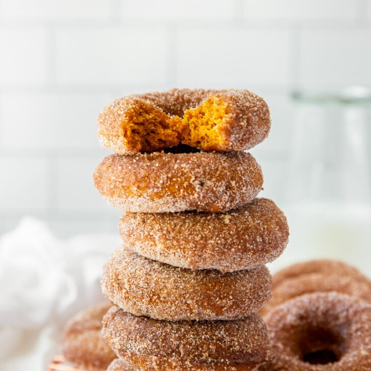 pumpkin donuts with cinnamon sugar in a stack with a bite taken out of the top donut