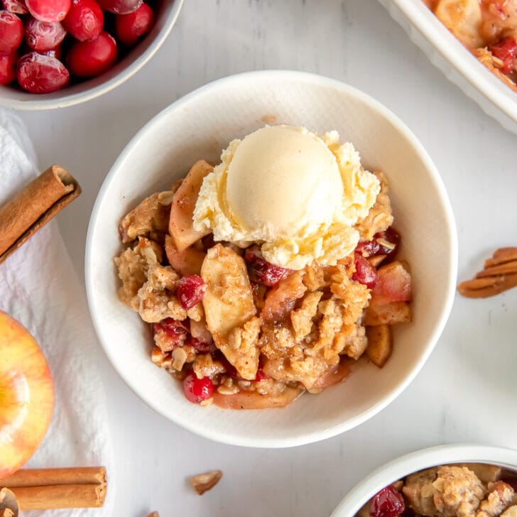 apple cranberry crisp in a white bowl with scoop of vanilla ice cream