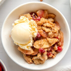 white bowl with apple cranberry crisp and scoop of vanilla ice cream