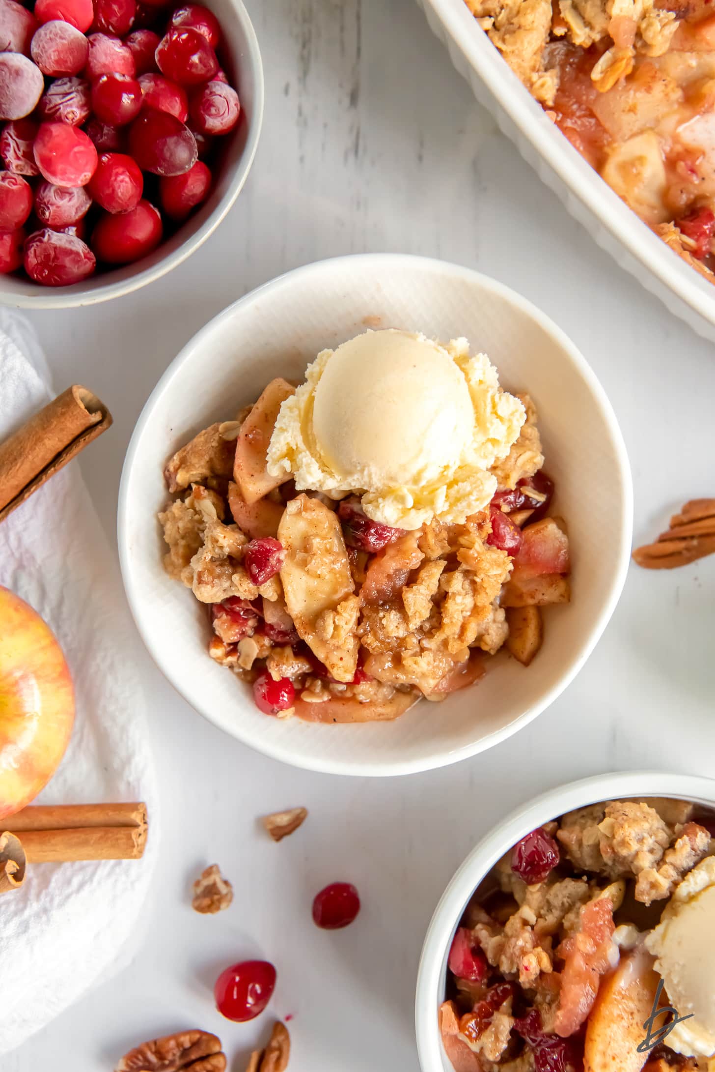 white bowl with apple cranberry crisp and scoop of vanilla ice cream.