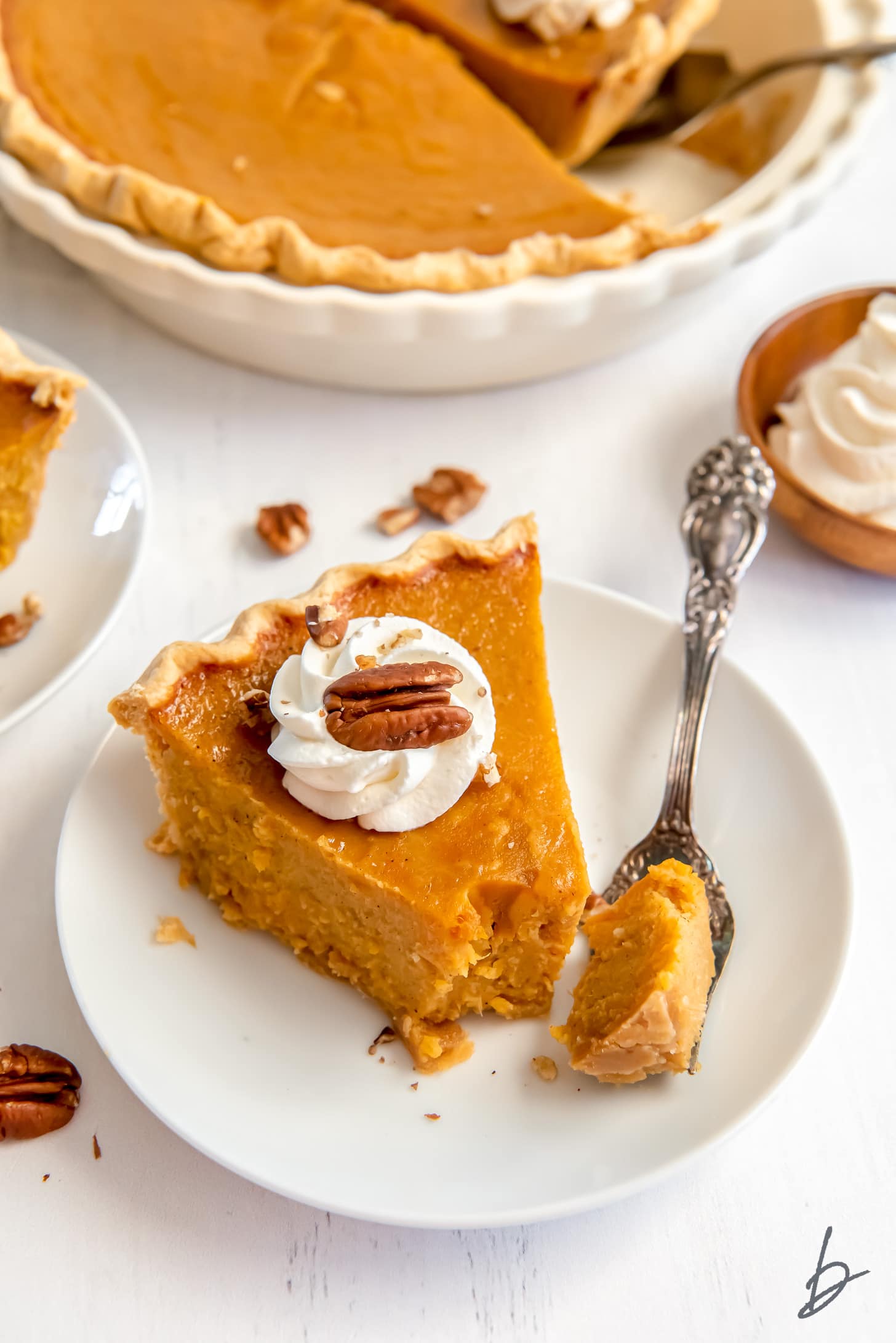 white round plate with slice of sweet potato pie garnished with whipped cream and pecan with fork taking bite