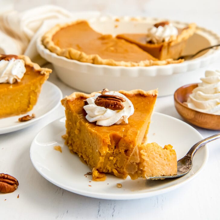 slice of bourbon sweet potato pie garnished with whipped cream and pecan and fork taking a bite of pie