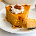 slice of sweet potato pie garnished with whipped cream and pecans and fork taking a bite