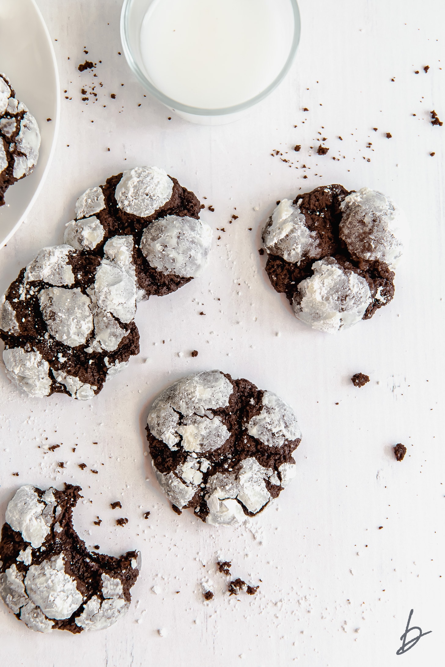 chocolate crinkle cookies on a white surface next to glass of milk