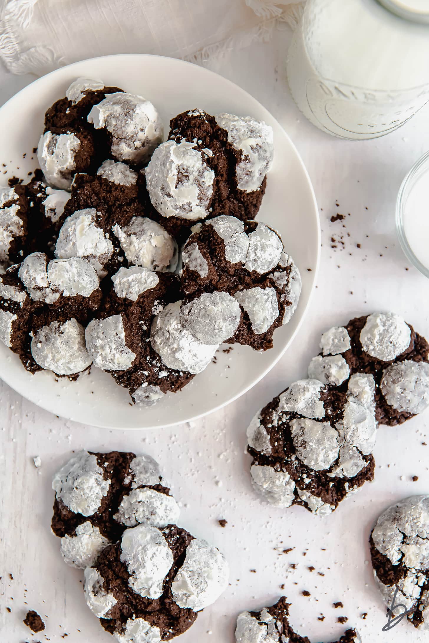 chocolate crinkle cookies  on white round plate next to more cookies and glass of milk