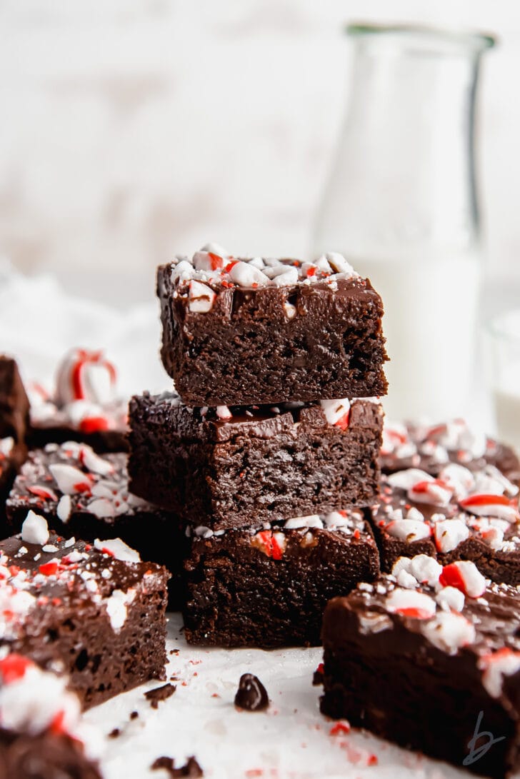 stack of three fudgy chocolate peppermint brownies with glass milk bottle and more brownies behind the stack