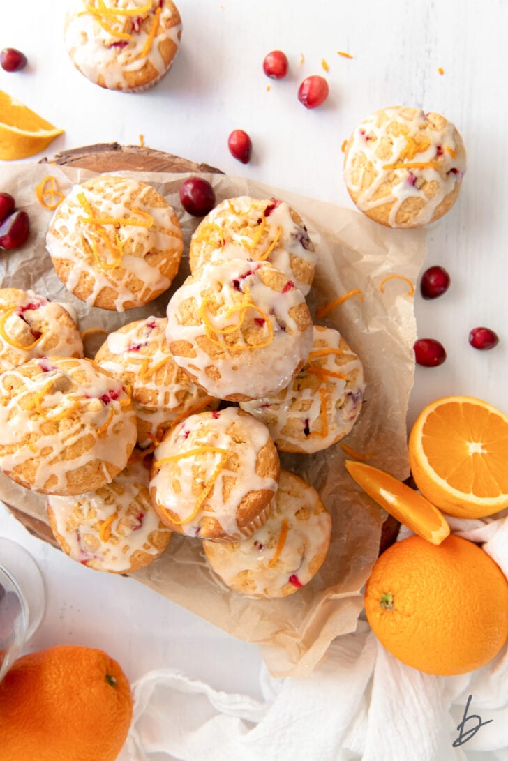 cranberry orange muffins with glaze in a pile next to fresh cranberries and orange slices