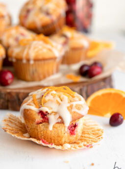 cranberry orange muffin with glaze and orange zest on open paper muffin liner