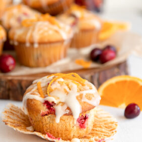 cranberry orange muffin with glaze and orange zest on open paper muffin liner.