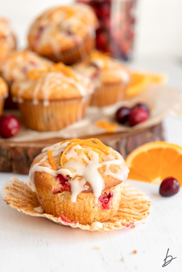cranberry orange muffin with glaze and orange zest on open paper muffin liner