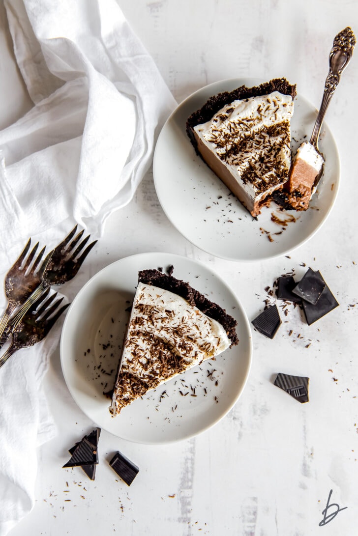 two plates each with a slice of chocolate cream pie with whipped cream and chocolate shavings
