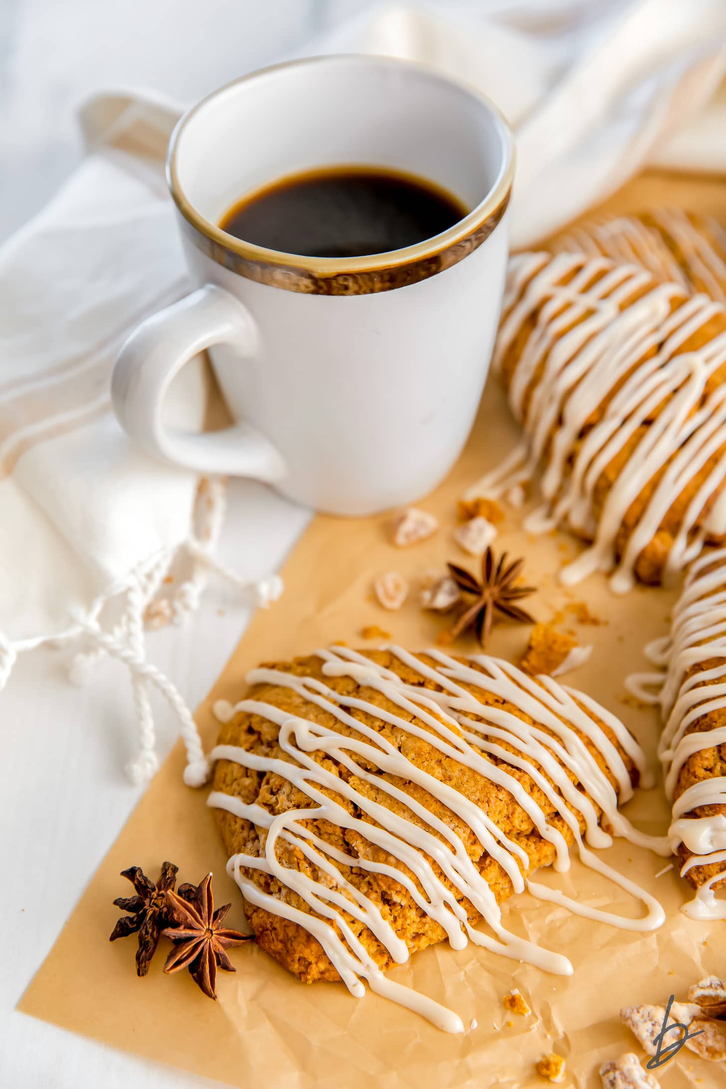 gingerbread scone with maple glaze on parchment paper next to anise star and white mug of coffee