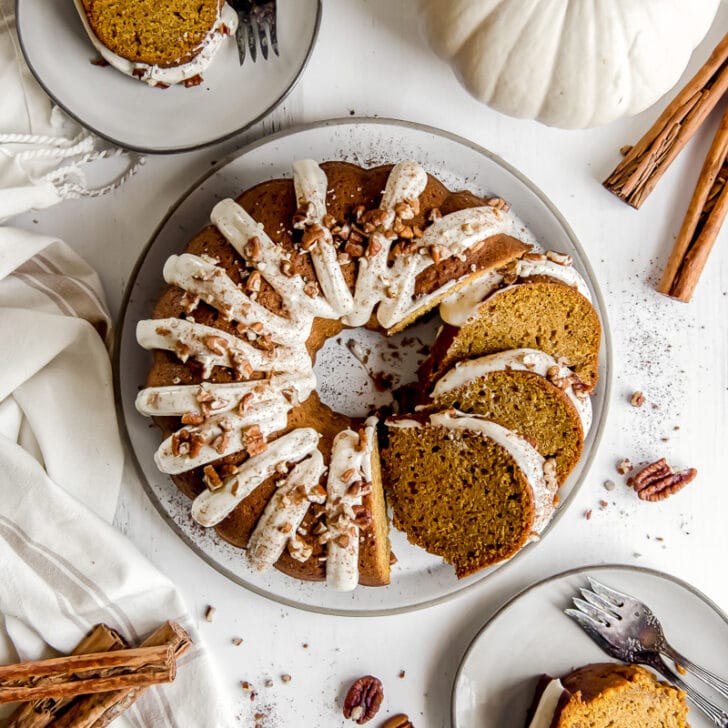pumpkin bundt cake with cream cheese frosting on plate with three slices cut and leaning on cake