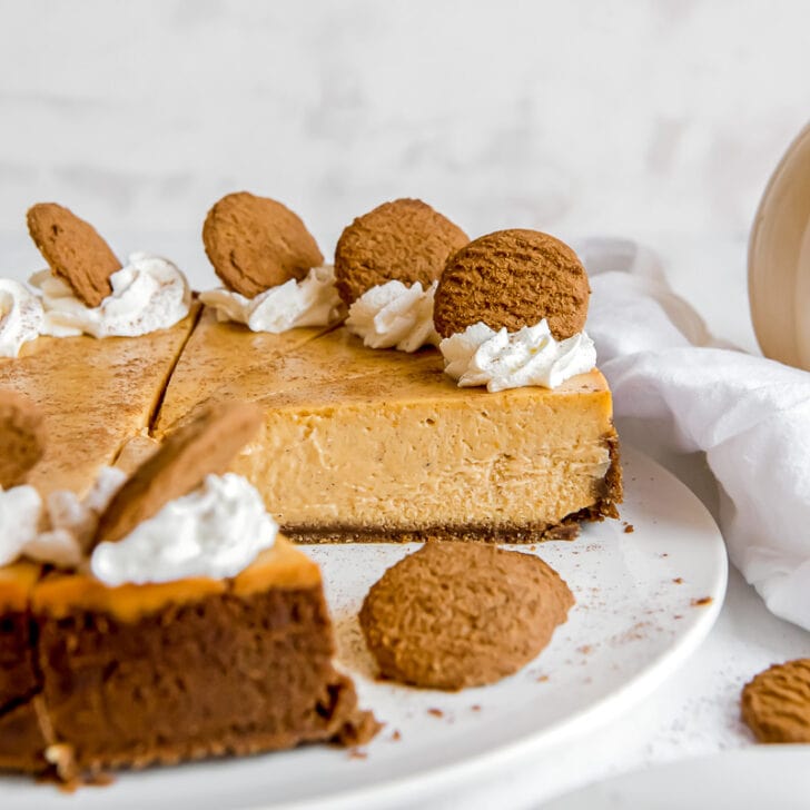 pumpkin cheesecake slice part of full cake garnished with whipped cream and gingersnap cookies