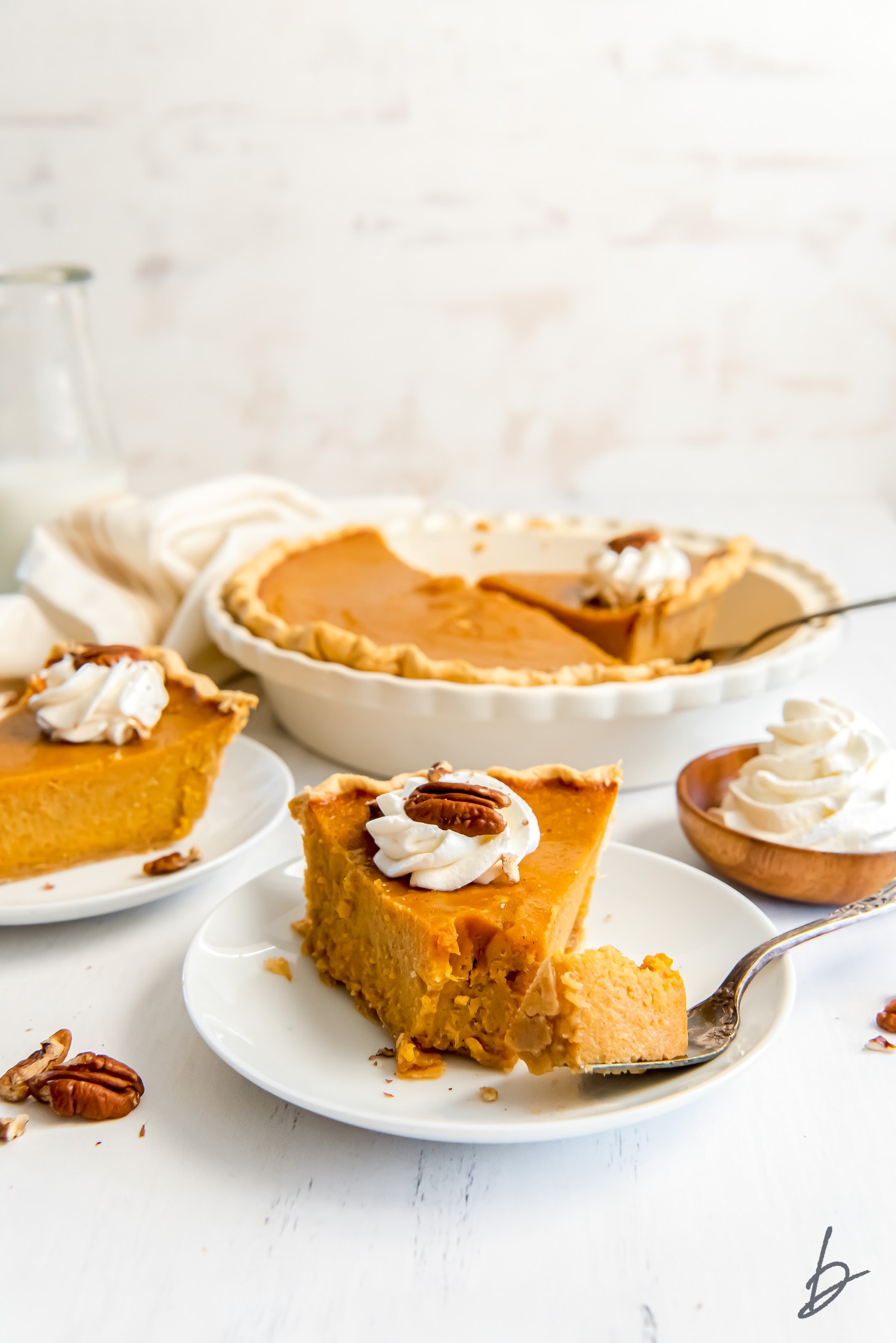 slice of sweet potato pie on white round plate with fork taking a bite and full pie behind plate