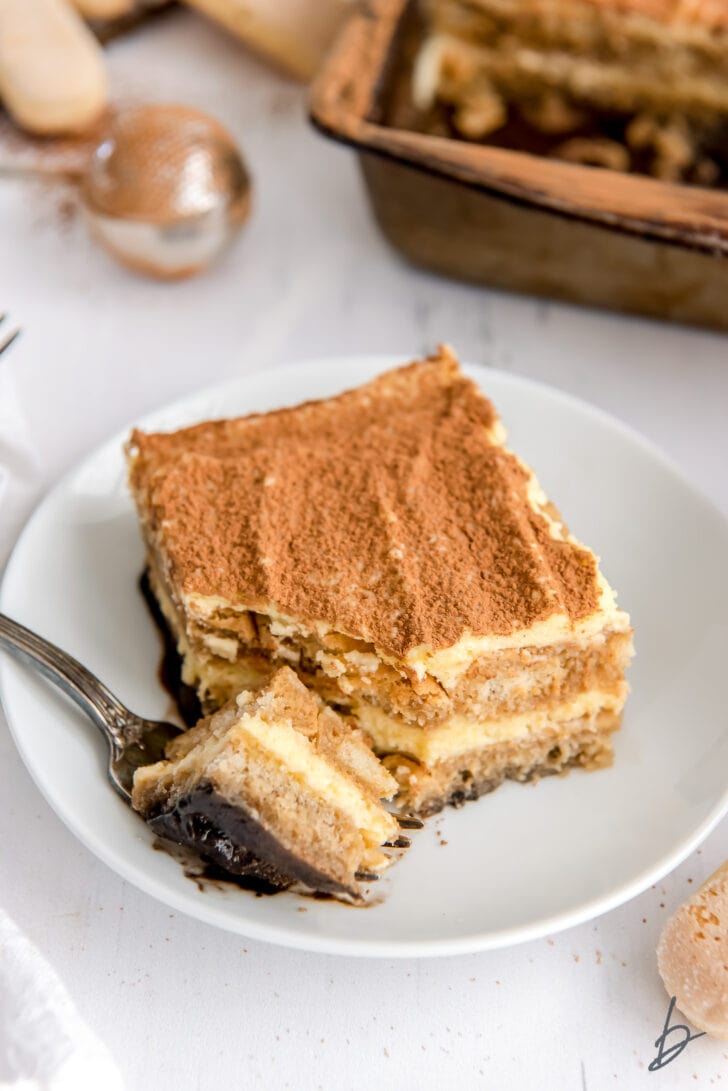 fork taking a bite out of piece of tiramisu on white round plate