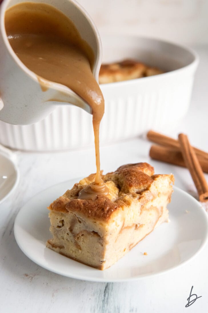 bourbon sauce being poured out of small pitcher onto piece of bread pudding on a plate