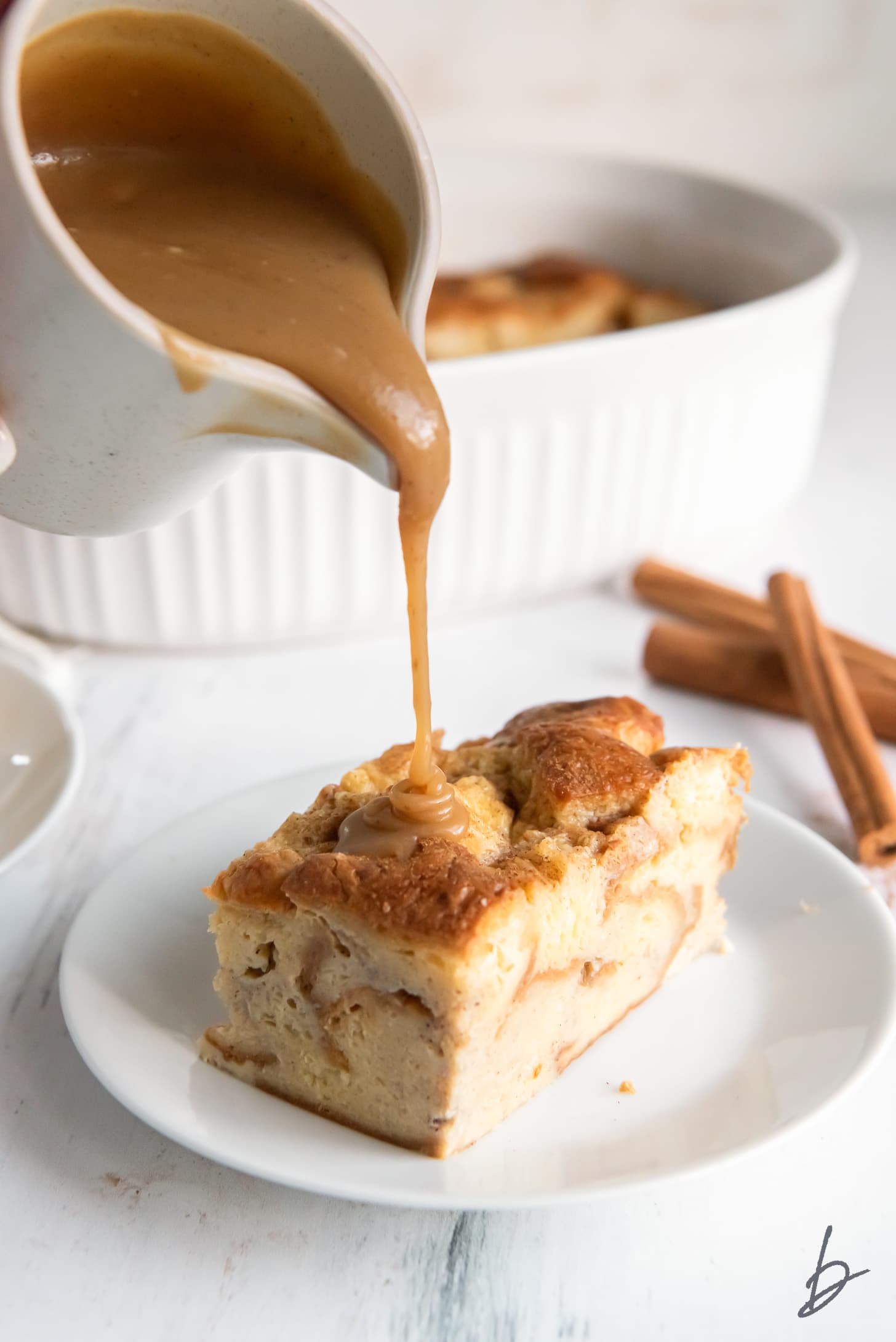 bourbon sauce being poured out of small pitcher onto piece of bread pudding on a plate