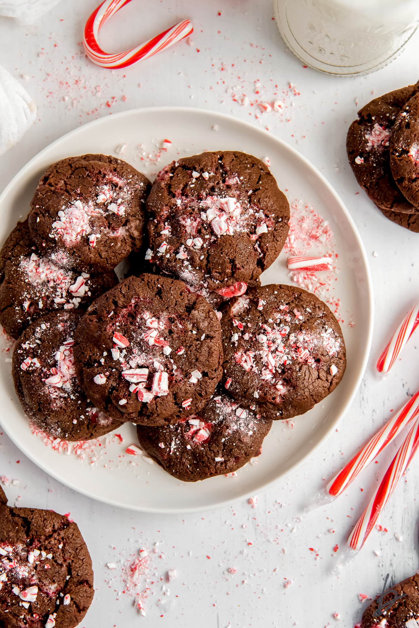 plate of double chocolate peppermint cookies with crushed peppermint next to a couple more cookies and candy canes.