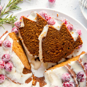 two slices of gingerbread bundt cake leaning up against cake with cream cheese frosting and sugared cranberries