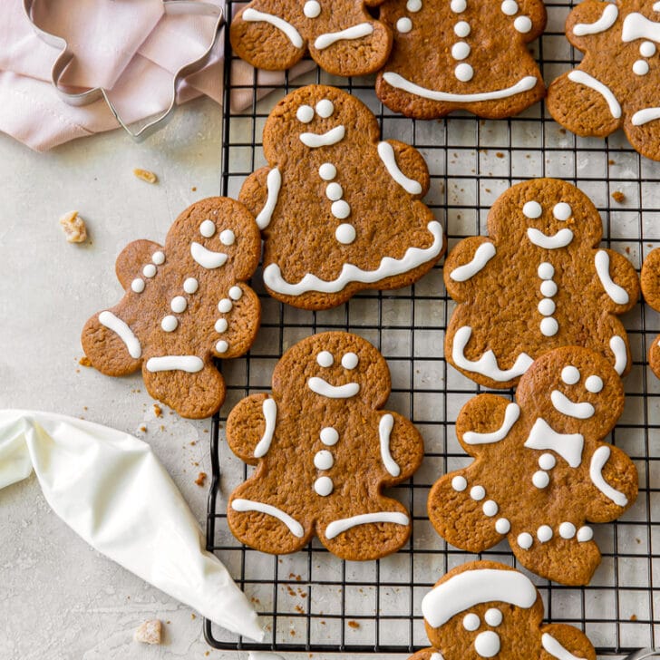 gingerbread man cookies decorated with icing on a wire cooling rack next to piping bag of icing