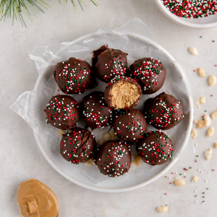 plate of peanut butter balls with chocolate and christmas sprinkles and one ball with a bite