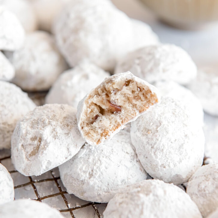 snowball cookie with a bite sitting on top of more powdered sugar covered cookies