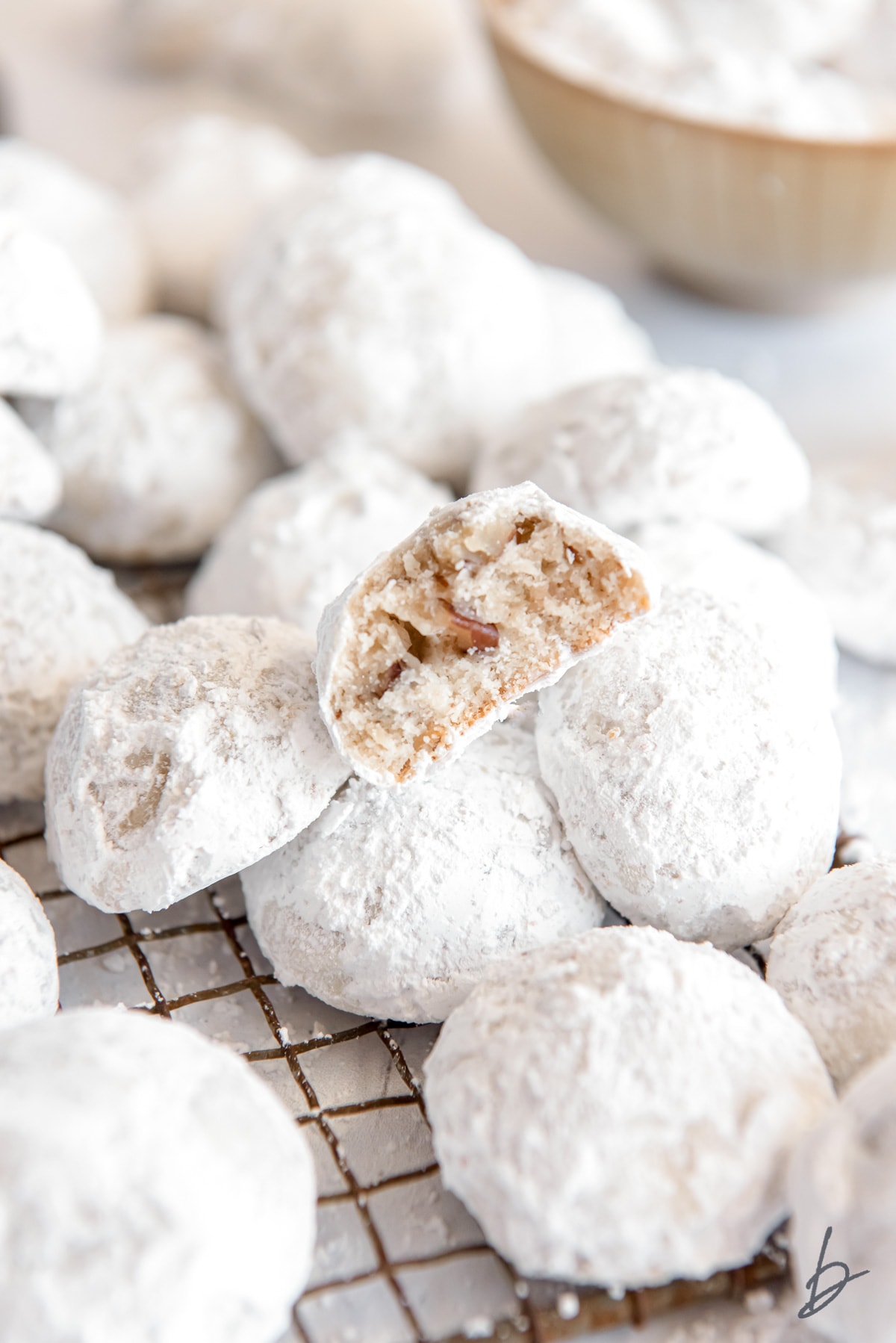 snow ball cookies in a pile on wire cooling rack and top cookie with a bite