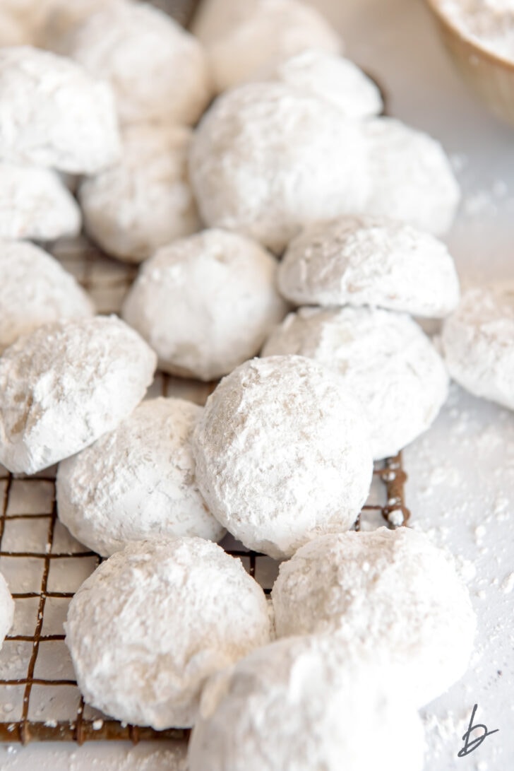 powdered sugar snowball cookies in a pile on antique wire cooling rack