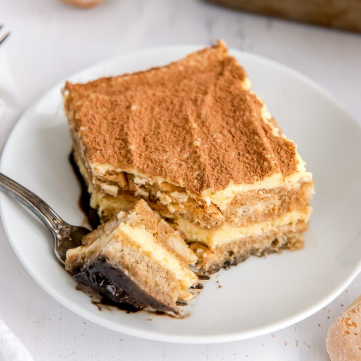 square slice of tiramisu dusted with cocoa powder and a fork taking a bite