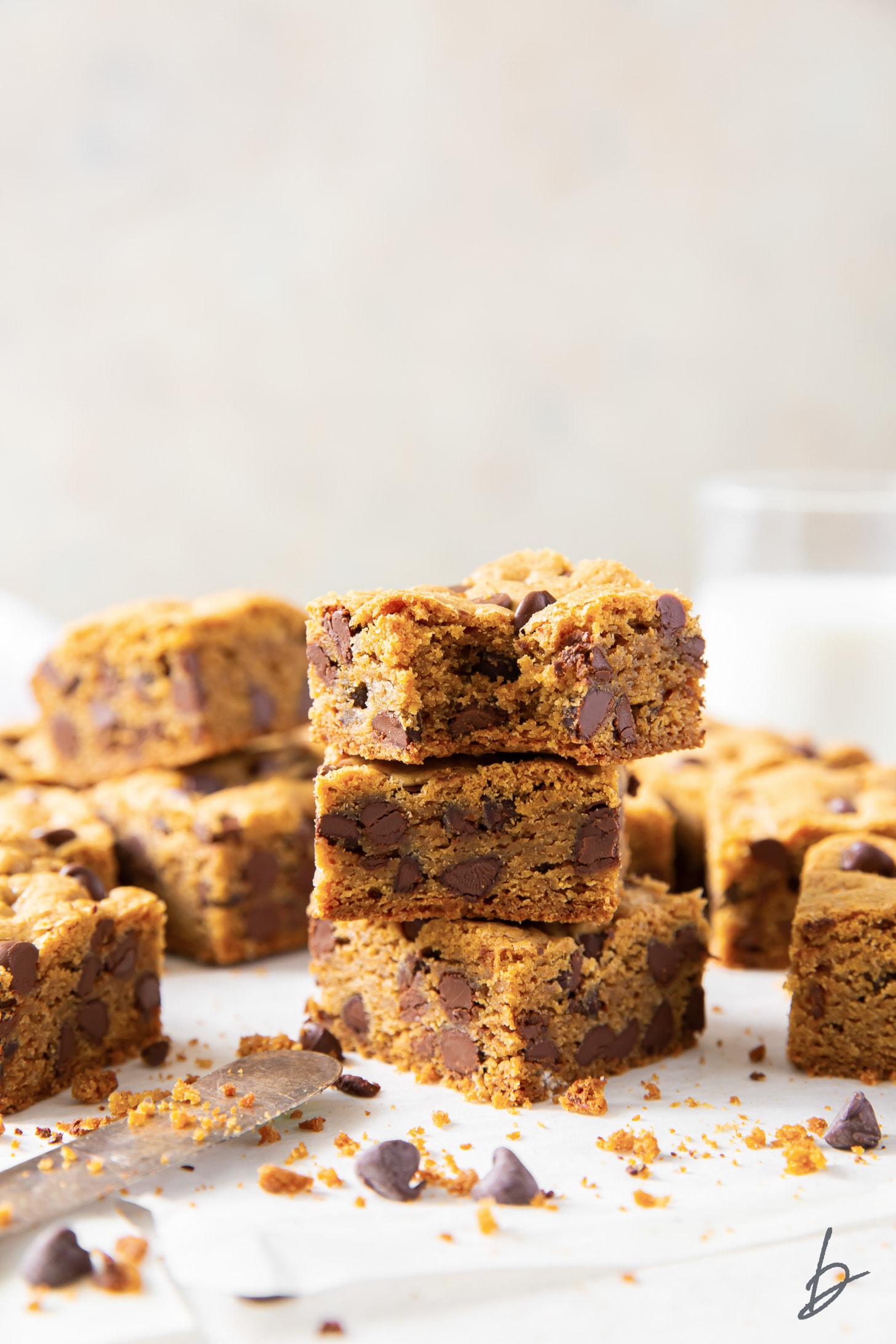 stack of three chocolate chip cookie bars next to more bars and glass bottle of milk