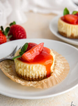 mini cheesecake with strawberry sauce on open paper muffin liner on white plate