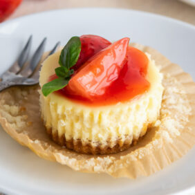 mini cheesecake with strawberry sauce on open paper liner on white round plate