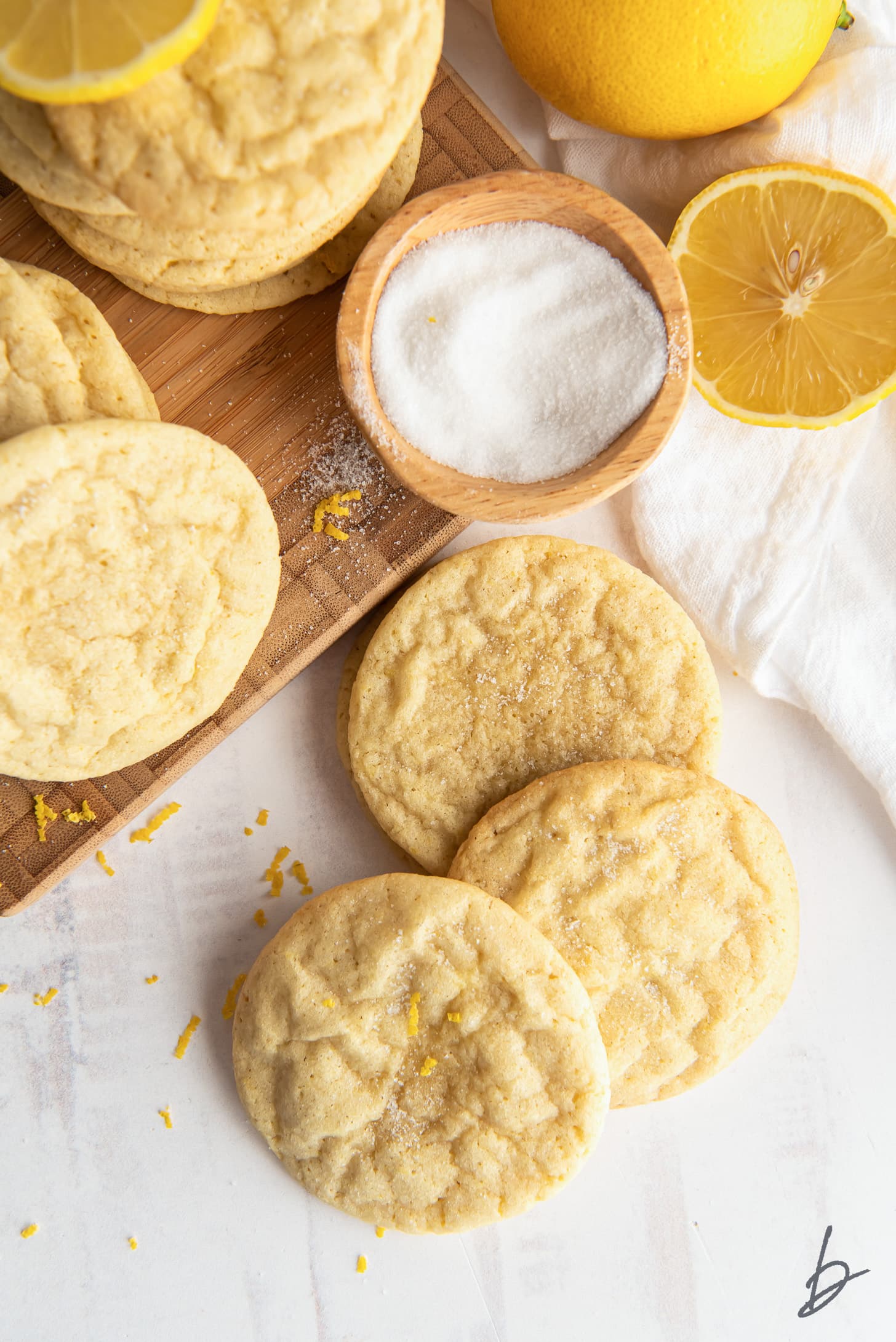 three lemon sugar cookies laid on top of each other next to pinch bowl of sugar and half a lemon
