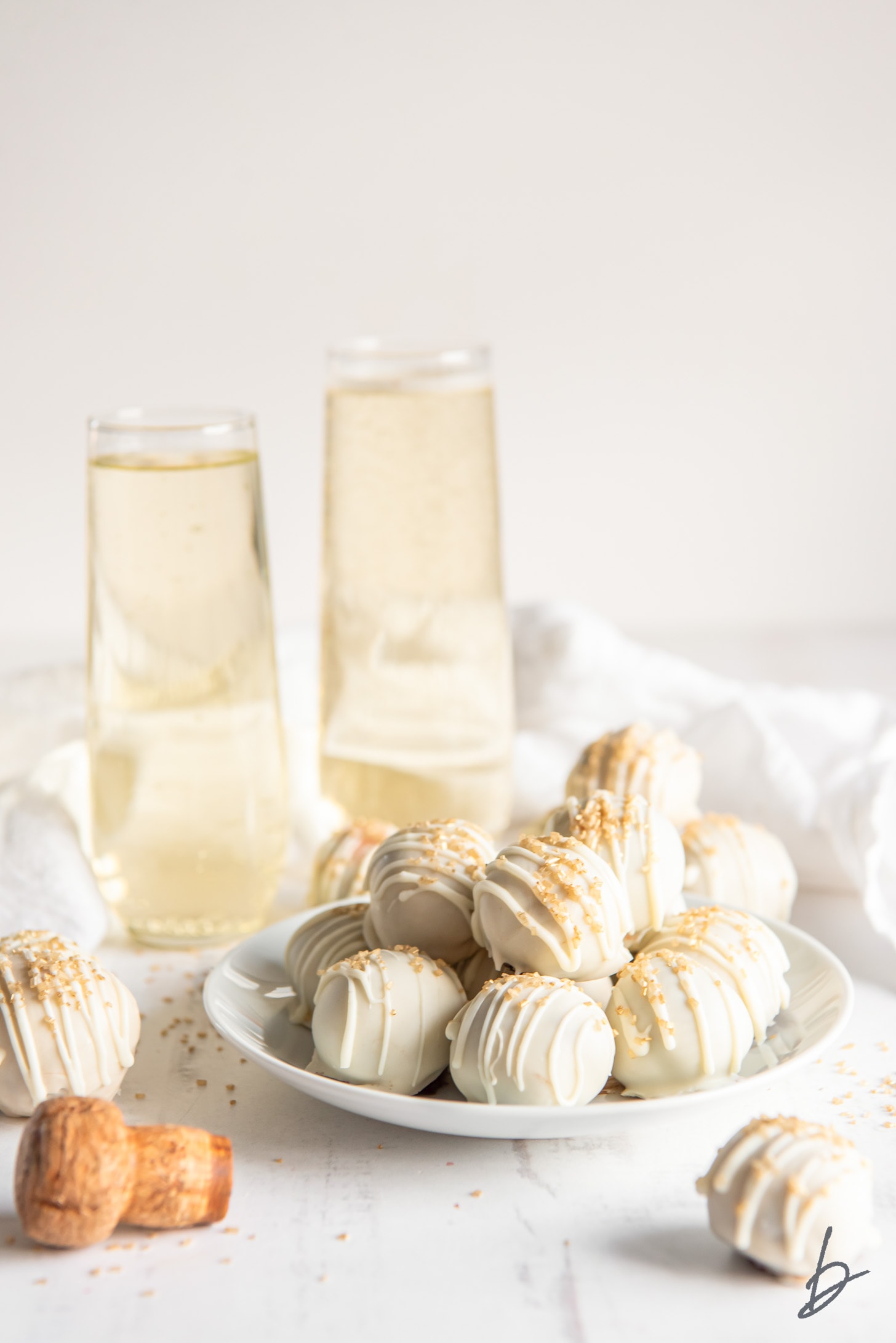 plate of white chocolate covered champagne truffles in front of two stemless champagne flutes
